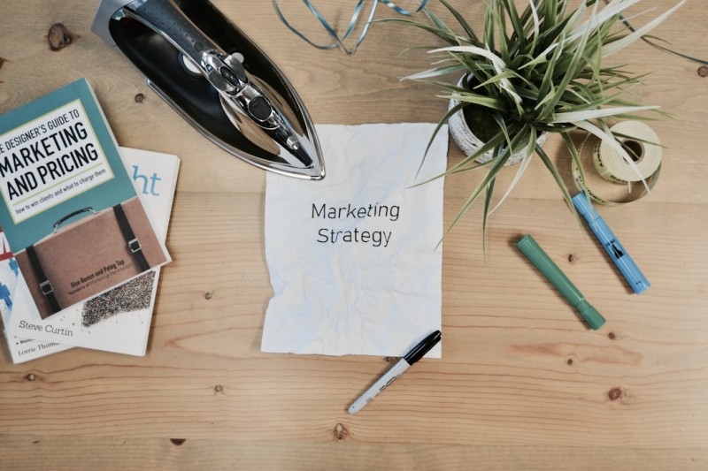 A wooden table with a marker, two highlights, a book about marketing, and a piece of paper with "Marketing Strategy" typed on it showing how BANT can help with marketing.