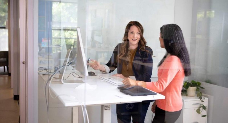 Two people looking at a computer at a standing desk discussing enterprise search's benefits.